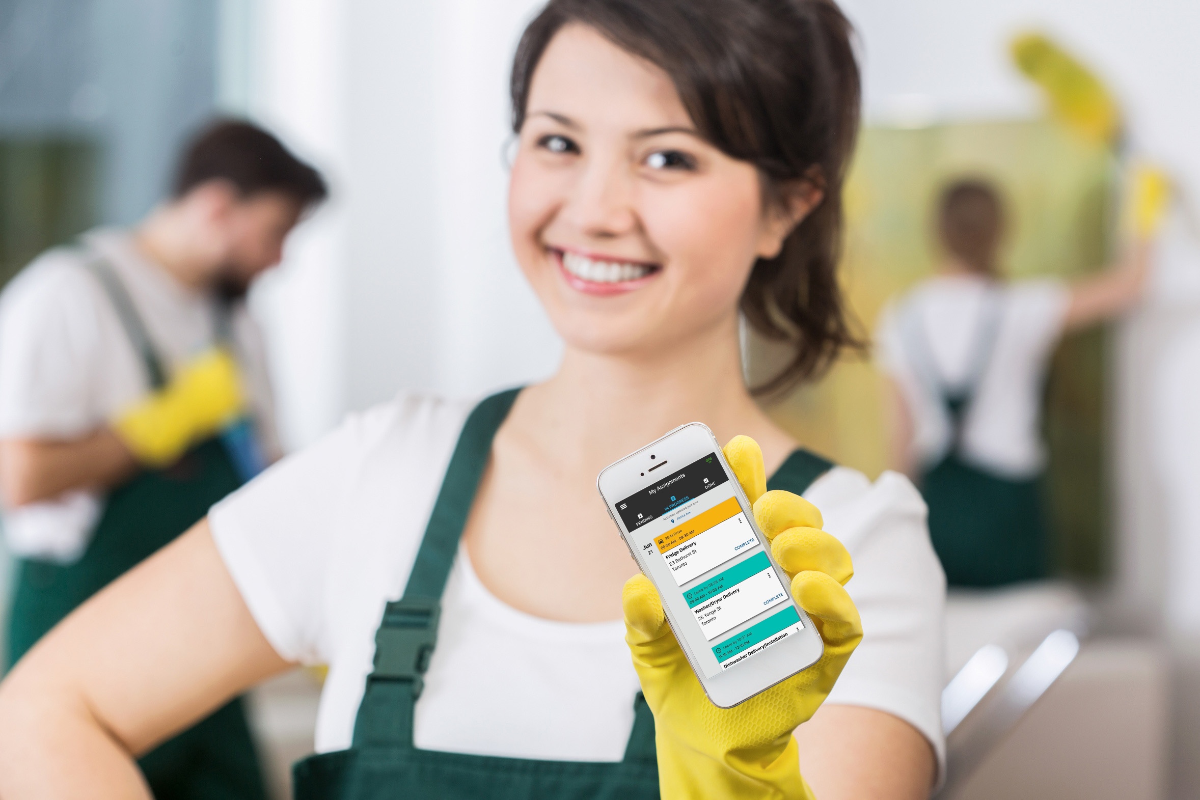 Young woman worker wearing yellow rubber gloves and holding a smartphone with Task Tracker app on the screen.