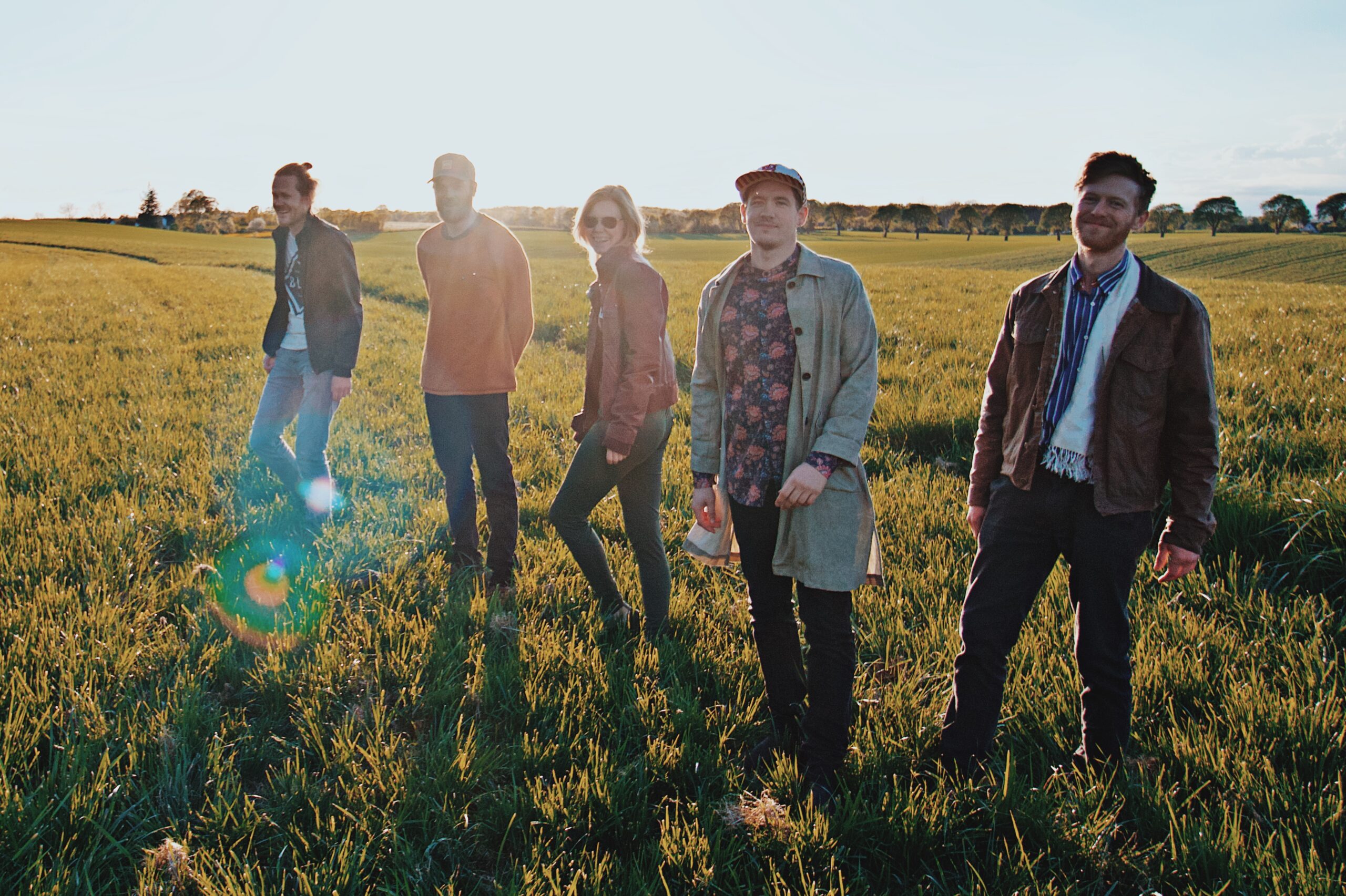 The five band members of Wild Forest stand in a grass field on a sunny day.