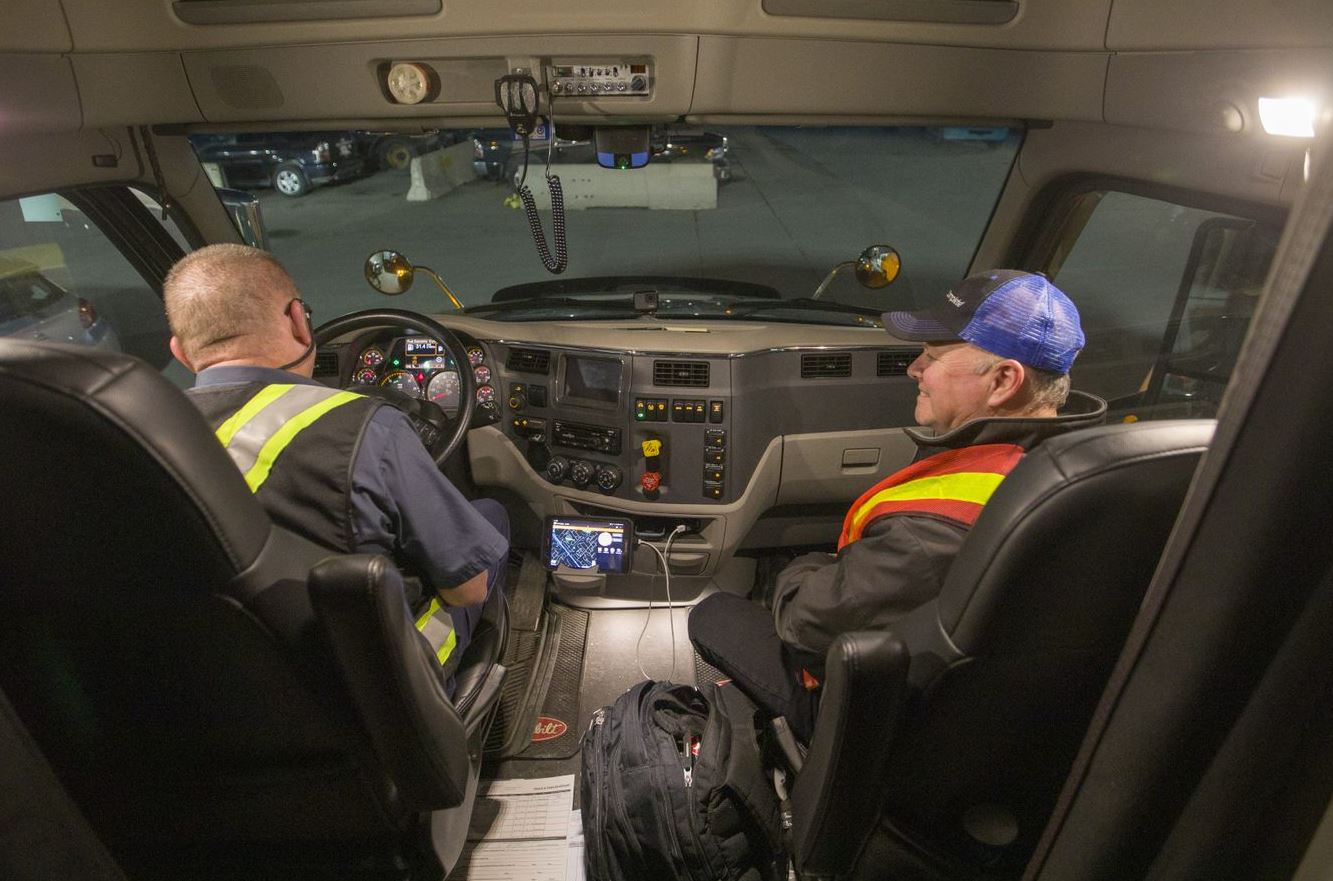 Truck driver filling out a report in a mobile device with Marc Moncion in the passenger seat.